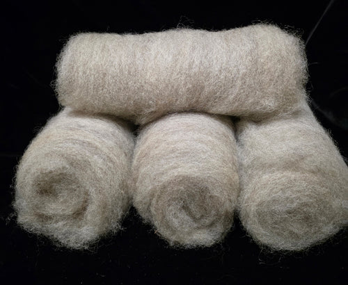 Four rolled batts of fluffy grey romney wool stacked on a solid black background.